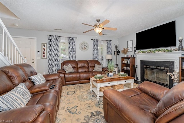 living room with a textured ceiling, ceiling fan, a glass covered fireplace, and stairway