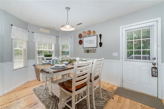 dining area with a textured ceiling, visible vents, light wood finished floors, and a wainscoted wall