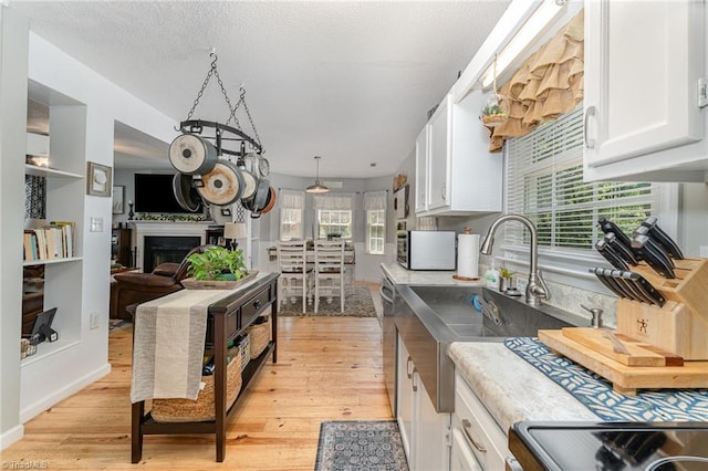 kitchen with a sink, a fireplace, light wood-style flooring, white cabinetry, and stainless steel microwave