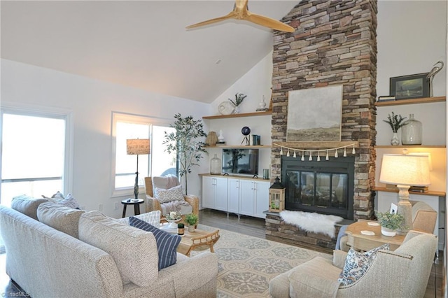 living area with high vaulted ceiling, ceiling fan, wood finished floors, and a stone fireplace