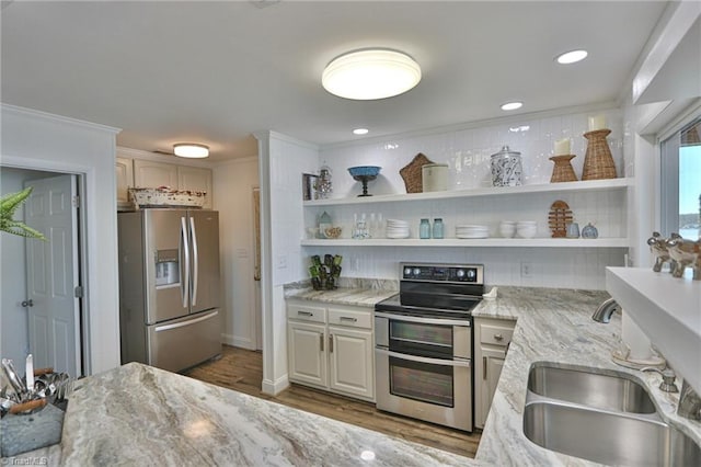 kitchen featuring open shelves, ornamental molding, stainless steel appliances, a sink, and light stone counters