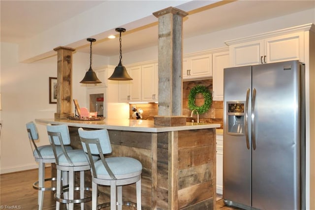 kitchen with white cabinetry, a breakfast bar area, dark wood finished floors, stainless steel refrigerator with ice dispenser, and decorative light fixtures