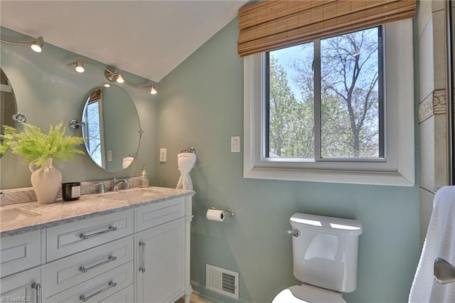 bathroom featuring vaulted ceiling, toilet, a sink, visible vents, and double vanity
