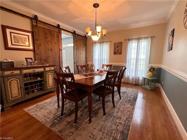 dining area with dark wood-type flooring, a barn door, a chandelier, and ornamental molding