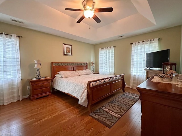 bedroom with a raised ceiling, ceiling fan, and dark hardwood / wood-style floors