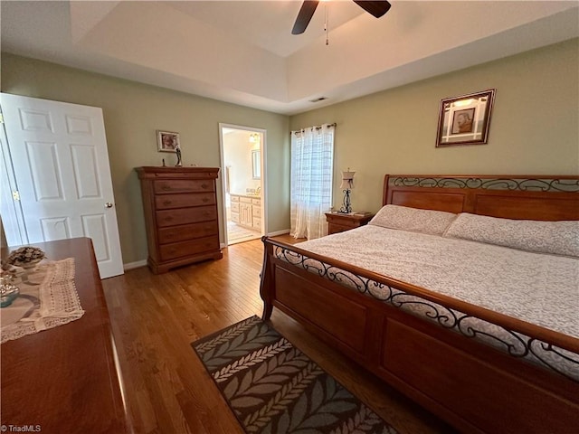 bedroom with ensuite bathroom, ceiling fan, a tray ceiling, and light hardwood / wood-style floors