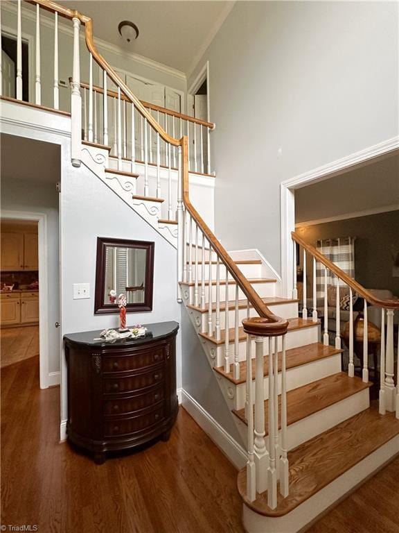 stairway with a towering ceiling, crown molding, and wood-type flooring