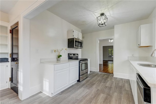 kitchen featuring appliances with stainless steel finishes, sink, a chandelier, white cabinets, and light hardwood / wood-style floors