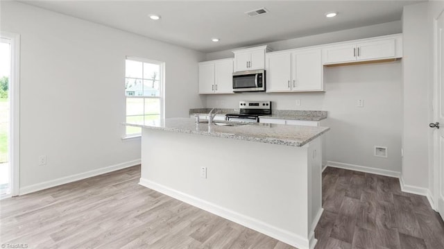 1529 String Dr, Winston-Salem, NC 27107 - kitchen featuring stainless steel appliances, white cabinets, a center island with sink, light wood finished floors, and light stone counters