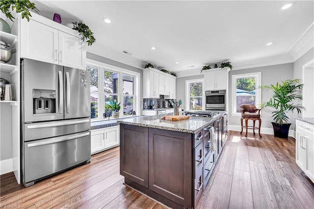 kitchen with appliances with stainless steel finishes, white cabinetry, crown molding, and wood-type flooring