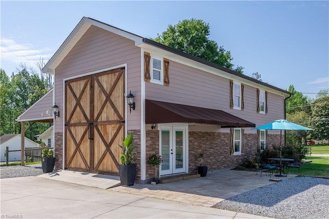 view of front of house featuring brick siding, french doors, a garage, an outdoor structure, and a patio area