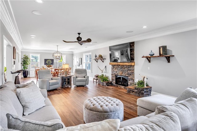 living area featuring ornamental molding, ceiling fan with notable chandelier, wood finished floors, a fireplace, and baseboards