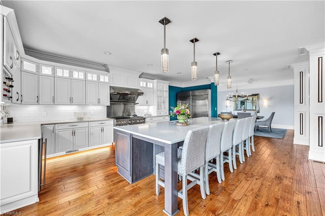 kitchen featuring ornamental molding, stainless steel refrigerator, under cabinet range hood, white cabinetry, and a kitchen breakfast bar