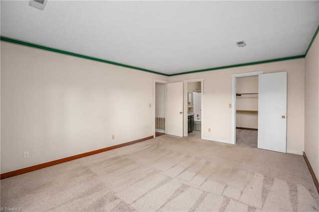 unfurnished bedroom featuring crown molding, ensuite bathroom, light carpet, a walk in closet, and a closet