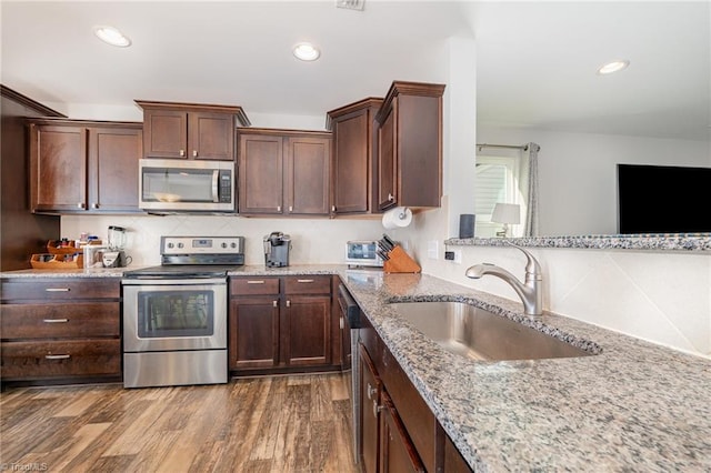 kitchen with sink, tasteful backsplash, appliances with stainless steel finishes, dark hardwood / wood-style flooring, and light stone countertops