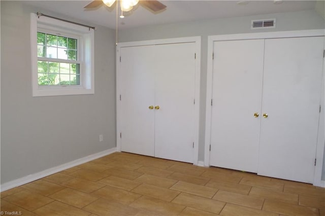 unfurnished bedroom with light tile patterned flooring, two closets, and ceiling fan