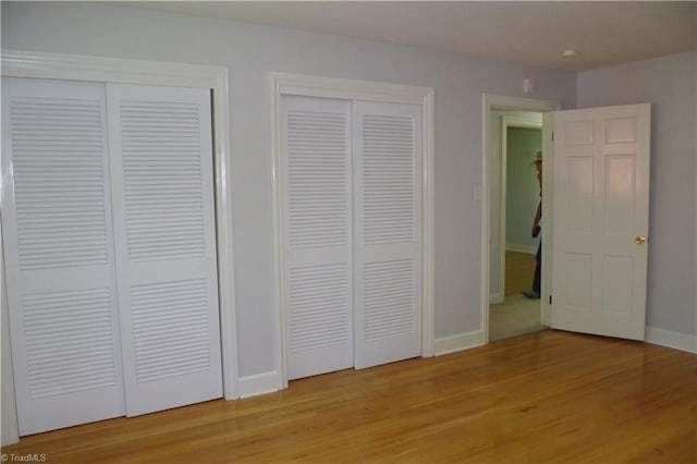 unfurnished bedroom featuring multiple closets and light wood-type flooring