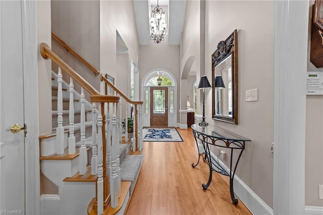 entryway with hardwood / wood-style flooring, a towering ceiling, and a notable chandelier