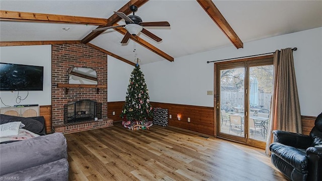 living room with wood walls, lofted ceiling with beams, ceiling fan, a fireplace, and light hardwood / wood-style floors