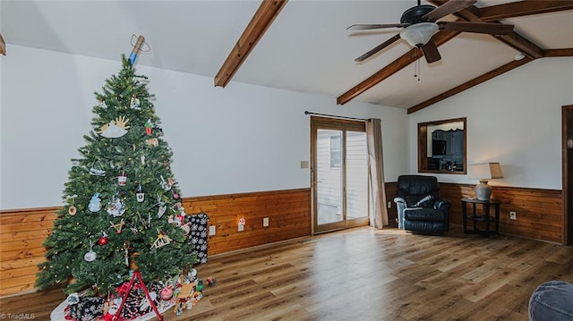 sitting room with vaulted ceiling with beams, ceiling fan, wood-type flooring, and wooden walls