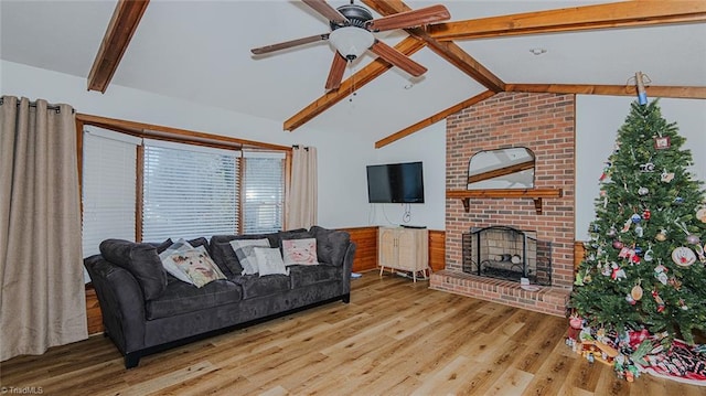 living room with ceiling fan, light hardwood / wood-style flooring, lofted ceiling with beams, and a brick fireplace