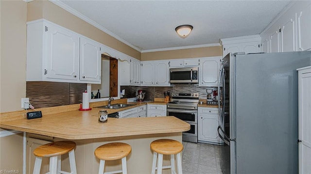 kitchen with white cabinets, ornamental molding, appliances with stainless steel finishes, a kitchen bar, and kitchen peninsula