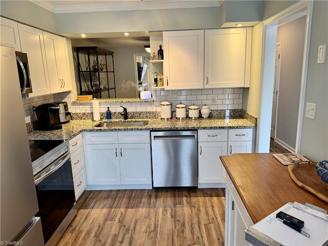 kitchen with dark stone countertops, ornamental molding, appliances with stainless steel finishes, hardwood / wood-style floors, and white cabinets