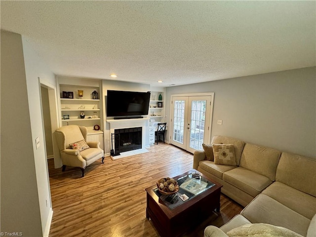 living room with french doors, built in features, hardwood / wood-style floors, and a textured ceiling