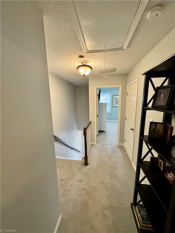 hallway with light carpet and a textured ceiling