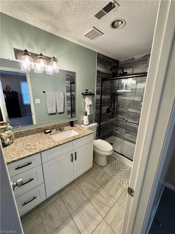 bathroom with vanity, toilet, a shower with door, and a textured ceiling