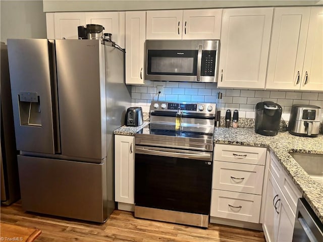 kitchen with stainless steel appliances, white cabinets, and light hardwood / wood-style flooring