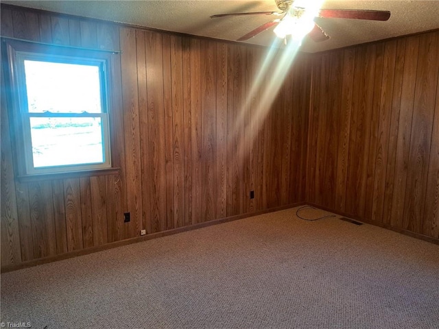 carpeted empty room featuring a textured ceiling, ceiling fan, and wood walls