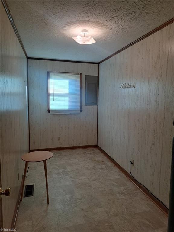 spare room featuring wooden walls, a textured ceiling, and ornamental molding