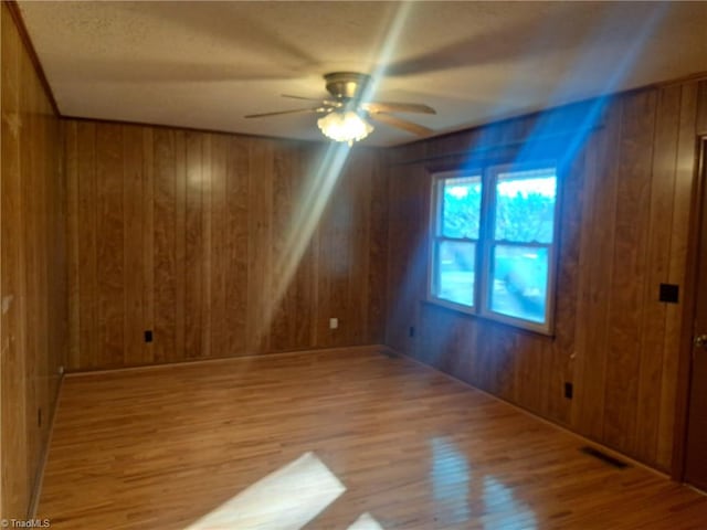 empty room with light wood-type flooring, ceiling fan, and wood walls