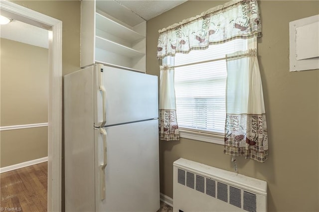 kitchen with hardwood / wood-style flooring, radiator heating unit, white fridge, and white cabinets