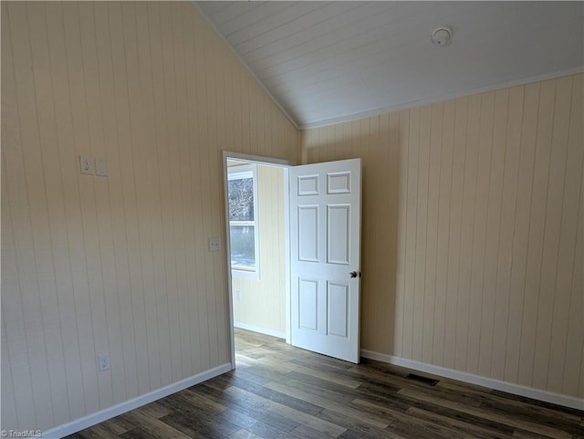 unfurnished room with dark wood-type flooring, visible vents, vaulted ceiling, wooden walls, and baseboards