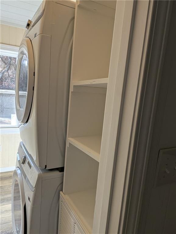 clothes washing area featuring light wood finished floors, laundry area, stacked washer and clothes dryer, and plenty of natural light