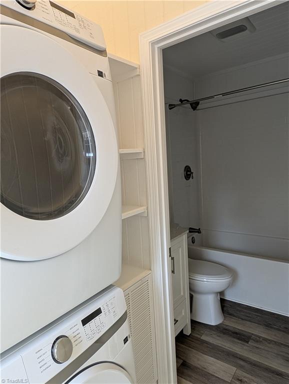 bathroom with visible vents, toilet, stacked washer / dryer, shower / bath combination, and wood finished floors