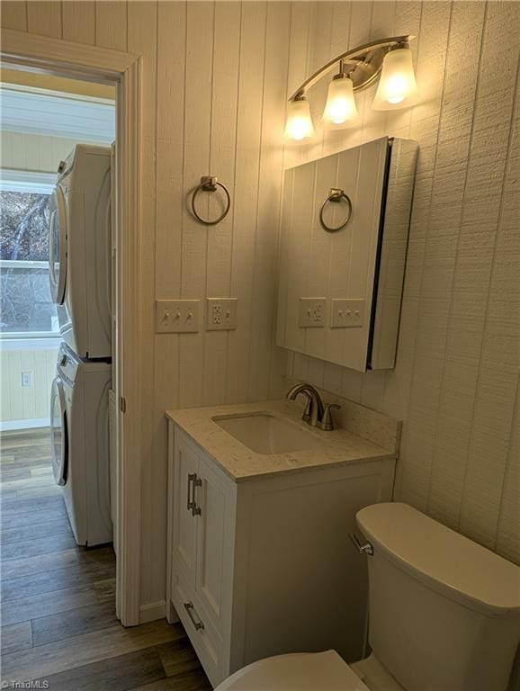 bathroom with toilet, stacked washer and dryer, wood finished floors, and vanity