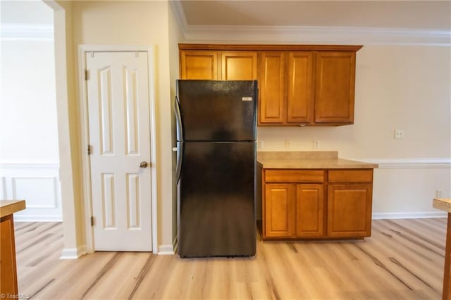 kitchen with black refrigerator, ornamental molding, and light hardwood / wood-style flooring