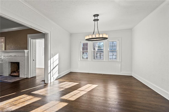 unfurnished dining area featuring dark hardwood / wood-style floors, a brick fireplace, ornamental molding, and a notable chandelier