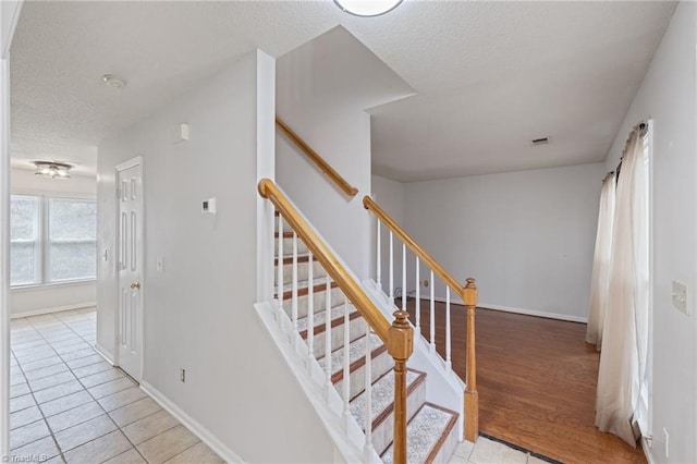 stairway featuring visible vents, a textured ceiling, baseboards, and wood finished floors