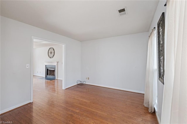 spare room featuring baseboards, a fireplace with flush hearth, visible vents, and wood finished floors