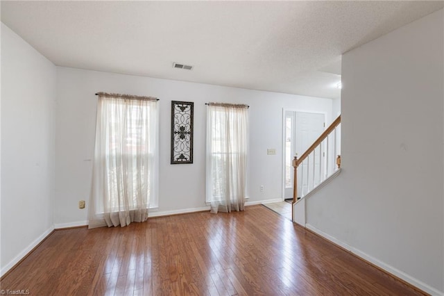 unfurnished room with hardwood / wood-style flooring, baseboards, stairway, and visible vents