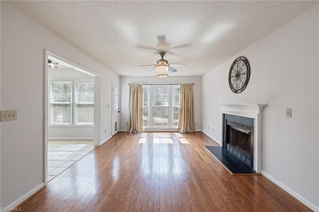 unfurnished living room featuring baseboards, ceiling fan, wood finished floors, a textured ceiling, and a fireplace