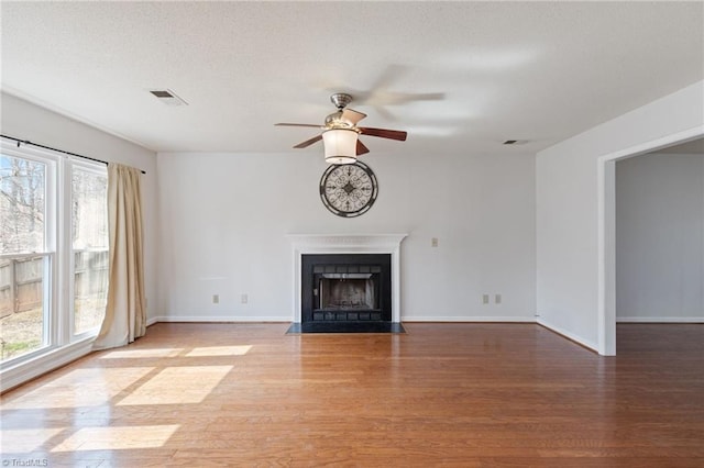 unfurnished living room featuring a fireplace with flush hearth, ceiling fan, baseboards, and wood finished floors