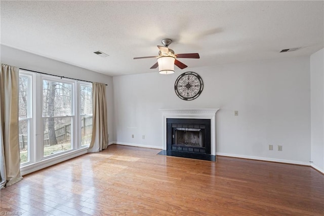 unfurnished living room featuring a fireplace, visible vents, a textured ceiling, wood finished floors, and baseboards