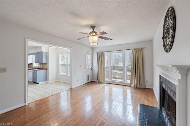 unfurnished living room with a fireplace with flush hearth, baseboards, ceiling fan, and light wood finished floors