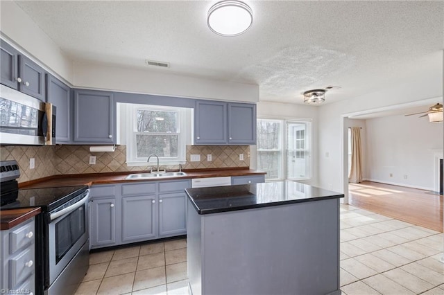 kitchen featuring light tile patterned floors, stainless steel appliances, dark countertops, visible vents, and a sink