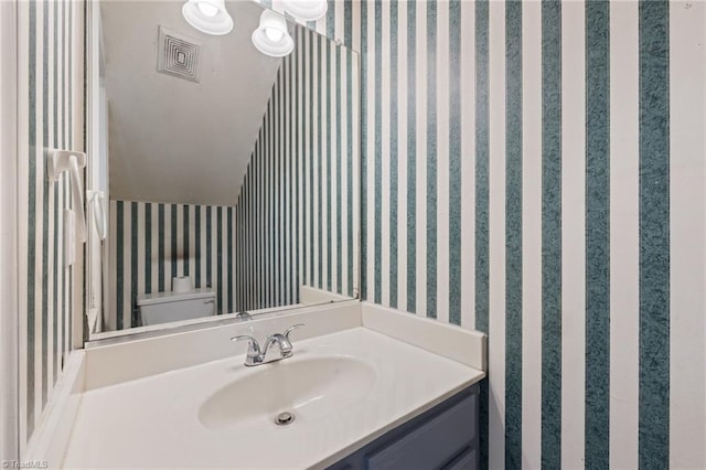 bathroom with visible vents, vanity, toilet, and wallpapered walls